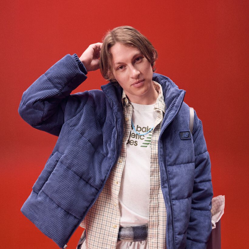 Man in a blue jacket scratching his head on a red backgroud.