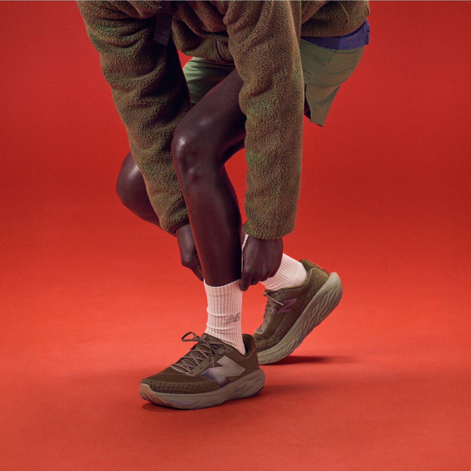 Young man bending over to tie his shoes on a red background.