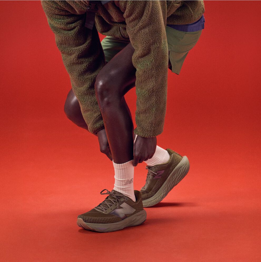 Young man bending over to tie his shoes on a red background.