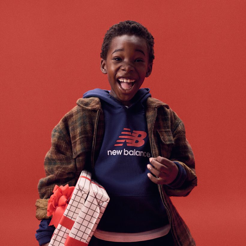 Young kid laughing while holding gifts on a red background.