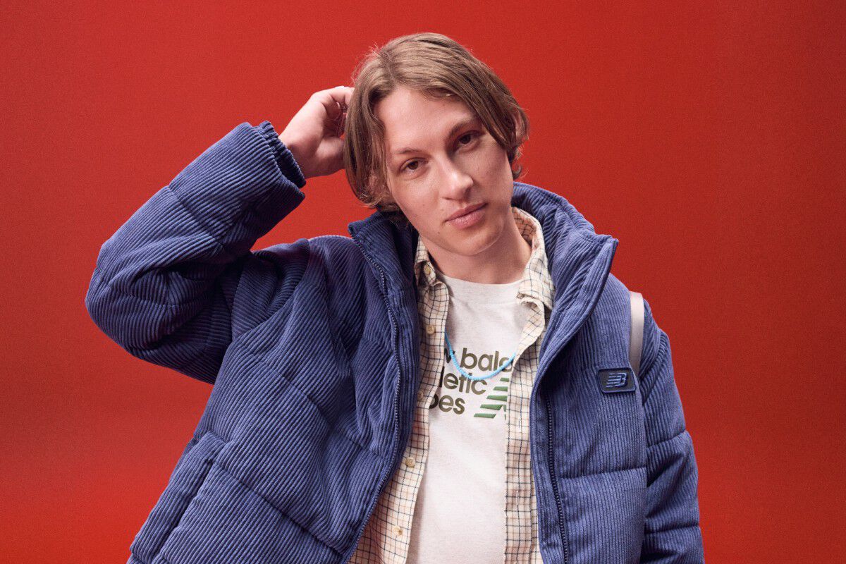 Young man in a blue coat scratching his head on a red background.